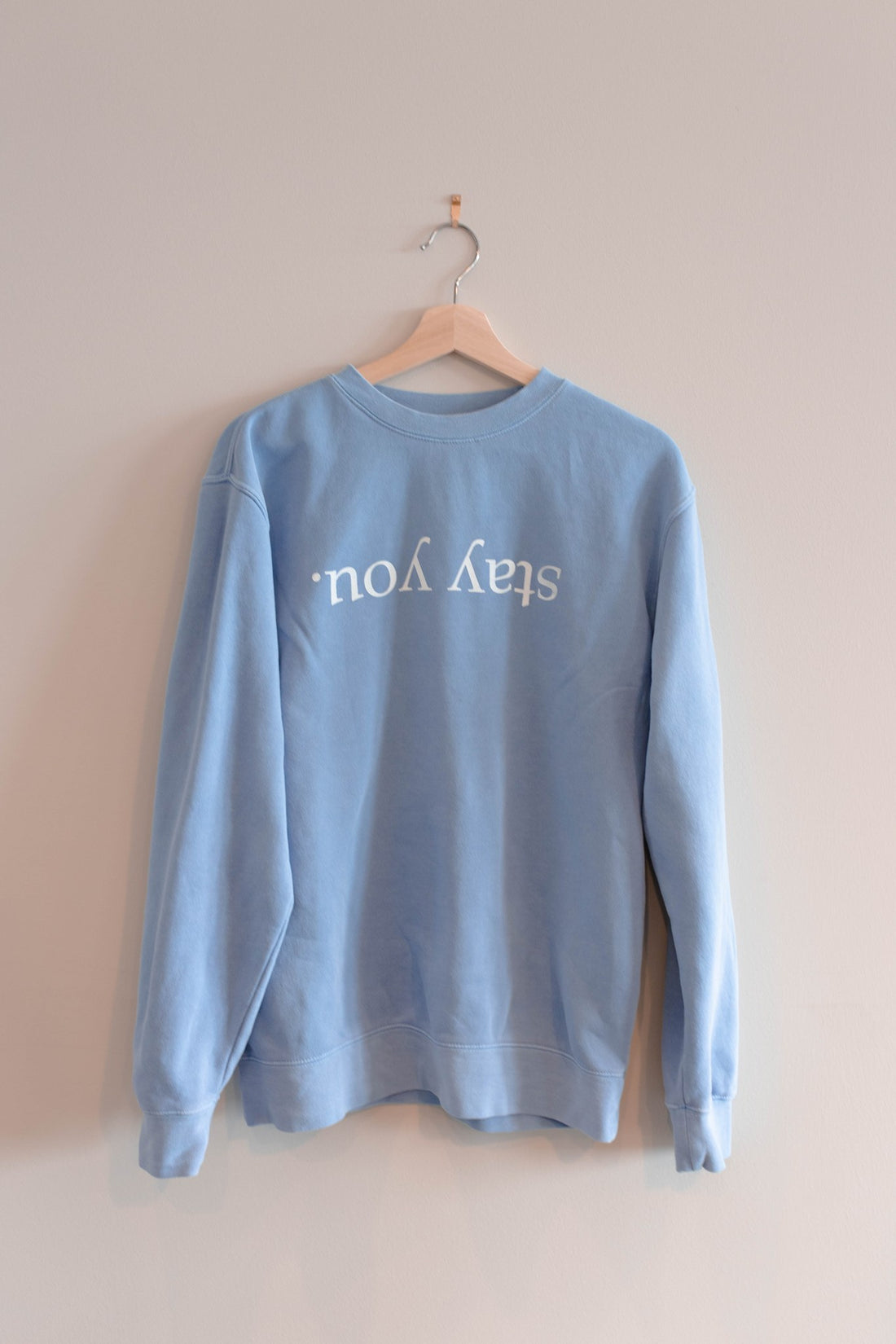 Stay You crewneck in Pigment Old South Blue hanging on a wooden hanger