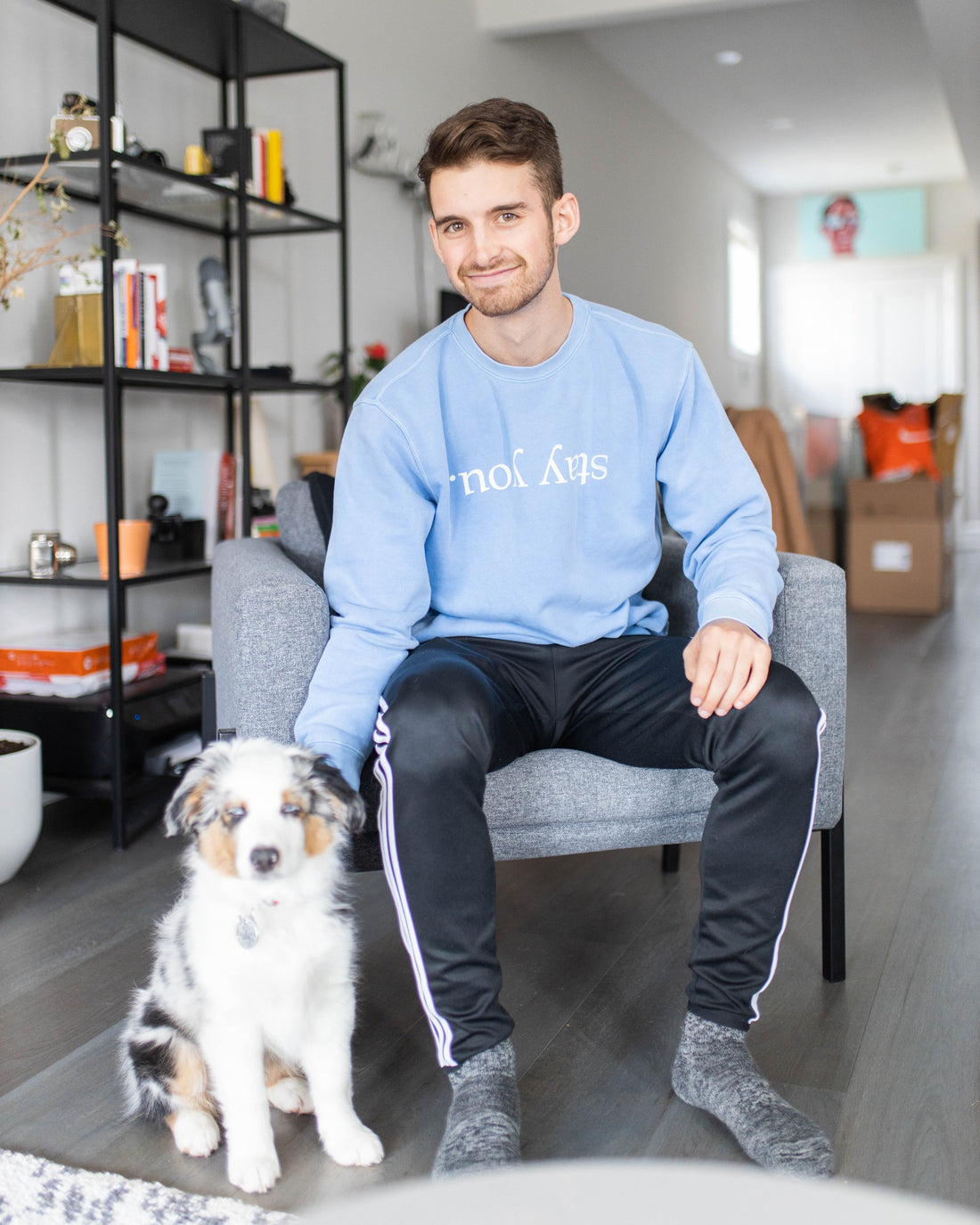 Model wearing the Stay You crewneck in Pigment Old South Blue, seated with a dog