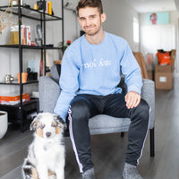 Model wearing the Stay You crewneck in Pigment Old South Blue, seated with a dog